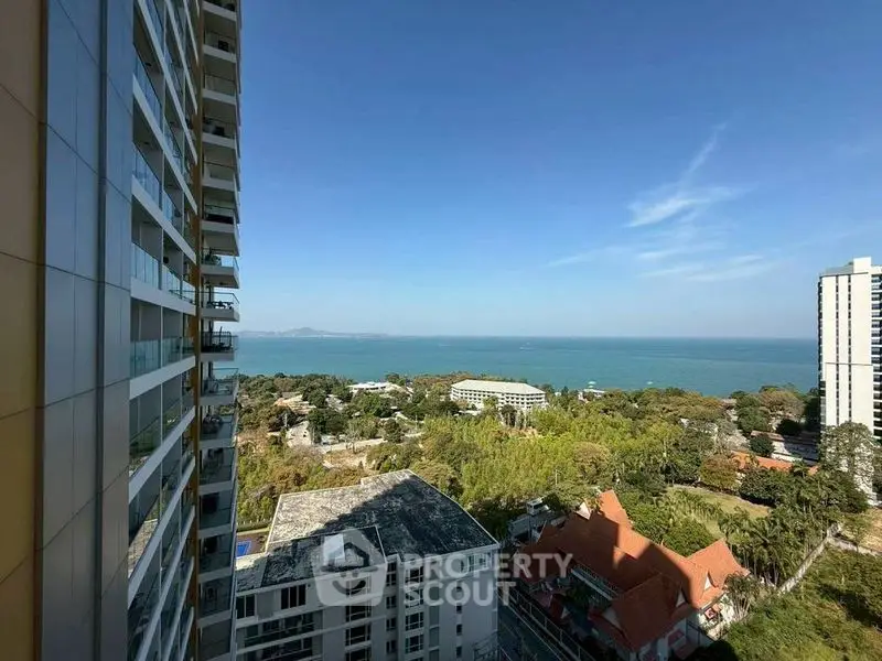 Stunning ocean view from high-rise balcony with lush greenery and clear blue sky.