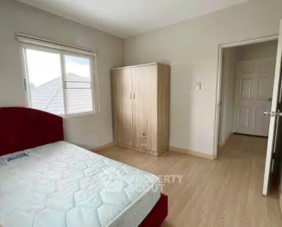 Bright bedroom with wooden flooring and large window, featuring a cozy bed and wardrobe.