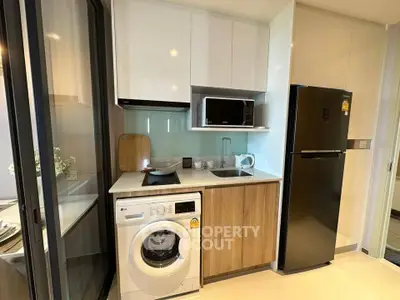 Modern compact kitchen with washing machine, microwave, and fridge in a stylish apartment.