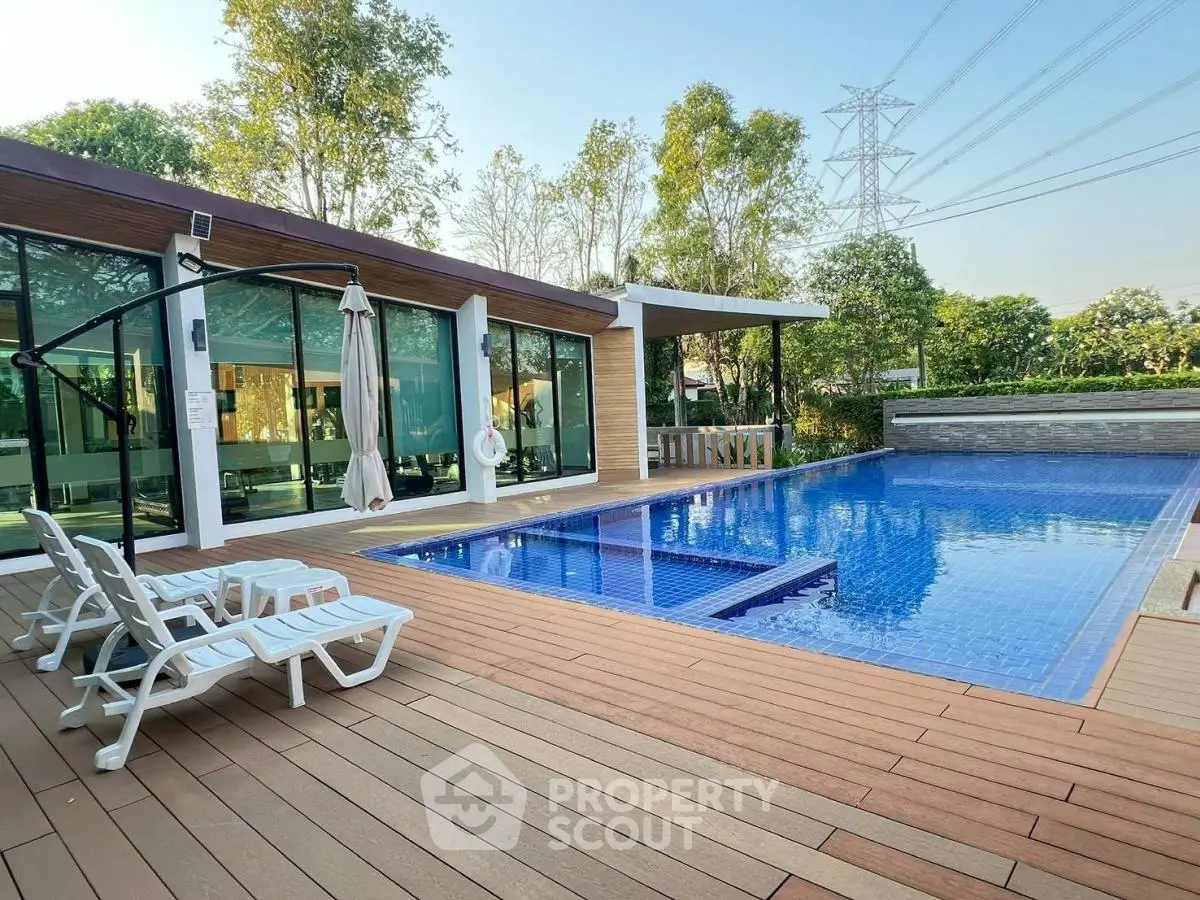 Luxurious modern poolside area with wooden deck and glass-walled building, perfect for relaxation and entertainment.