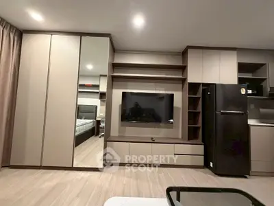 Modern living room with sleek cabinetry and flat-screen TV, featuring a glimpse into a stylish bedroom.