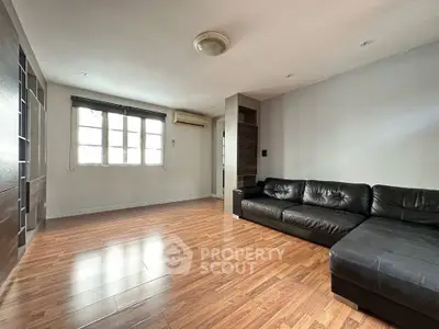 Spacious living room with wooden flooring and modern black leather sofa, perfect for relaxation.