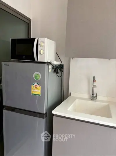 Compact kitchen with modern fridge, microwave, and sleek sink design.