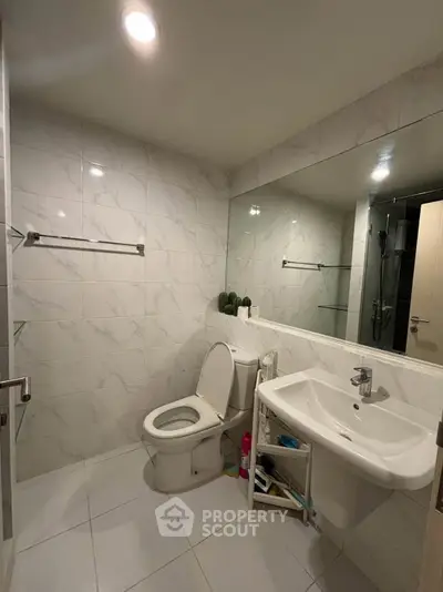 Modern bathroom with sleek white tiles and large mirror, featuring a toilet and sink.