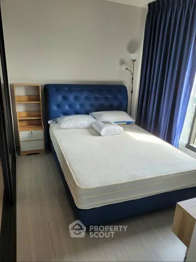 Modern bedroom with blue upholstered bed and natural light from large window.