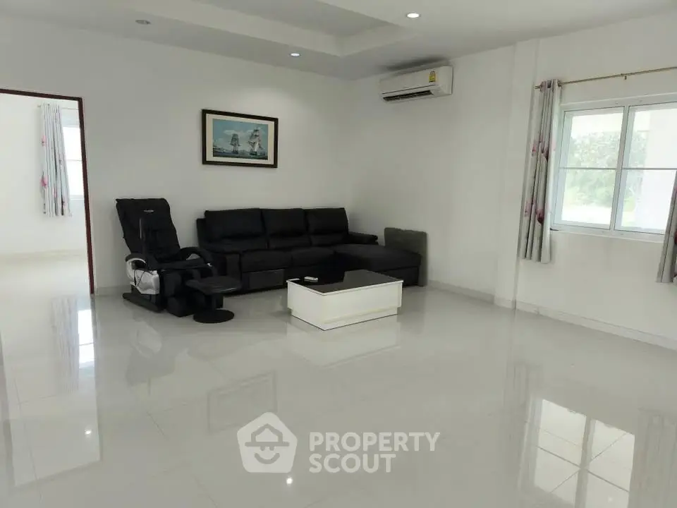 Spacious living room with modern black sofa and massage chair, bright natural light through large window.