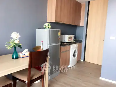 Modern kitchen with fridge, washing machine, and dining area in cozy apartment.