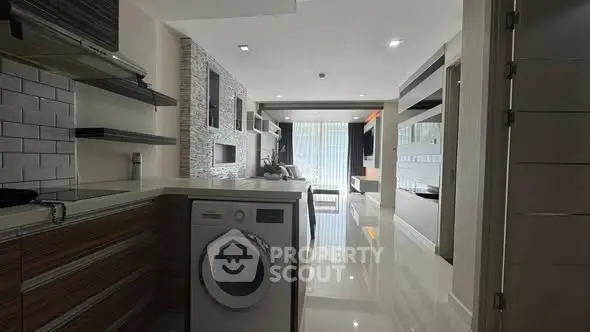 Modern open-plan living room with sleek kitchen and washing machine, featuring stylish decor and ample natural light.