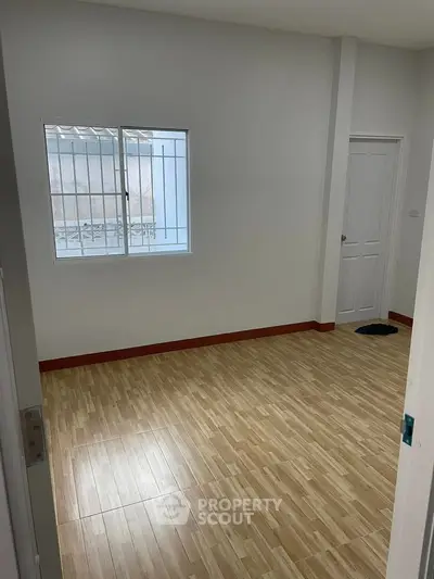 Spacious empty room with wooden flooring and window, ready for customization.