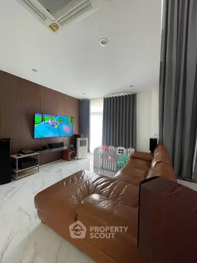 Spacious living room with modern decor and large leather sofa, featuring a wall-mounted TV and elegant curtains.