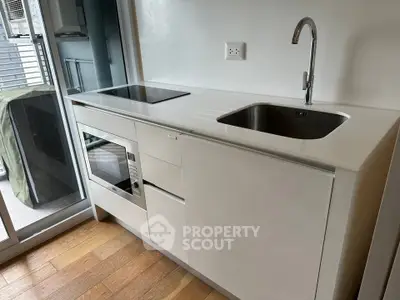 Modern kitchen with sleek white cabinetry and built-in appliances, featuring a compact design and wooden flooring.