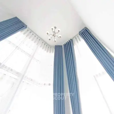 Elegant corner unit with high ceilings and modern chandelier, featuring floor-to-ceiling blue drapes.