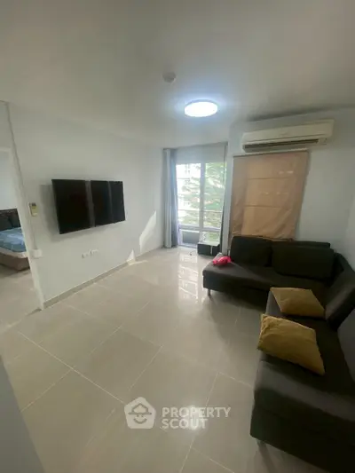 Modern living room with sleek sofa, wall-mounted TV, and large window offering natural light.