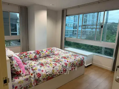 Bright bedroom with floral bedding and large windows offering a scenic view in a modern apartment.