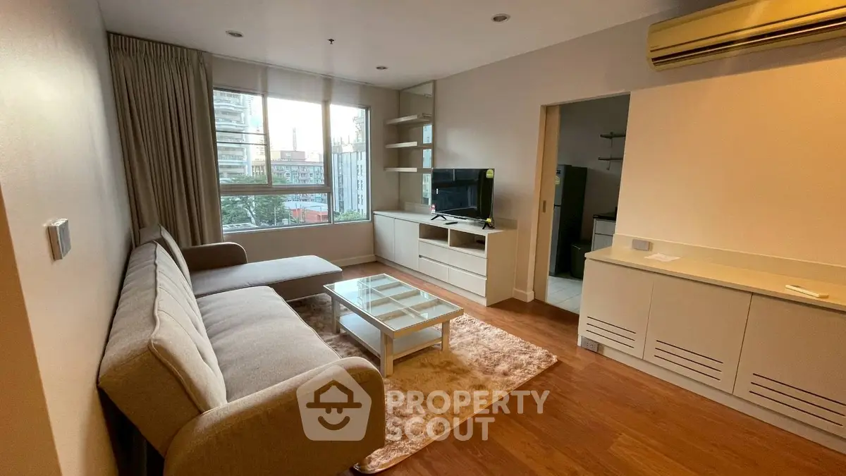 Modern living room with cozy sofa, TV, and large window view in urban apartment.
