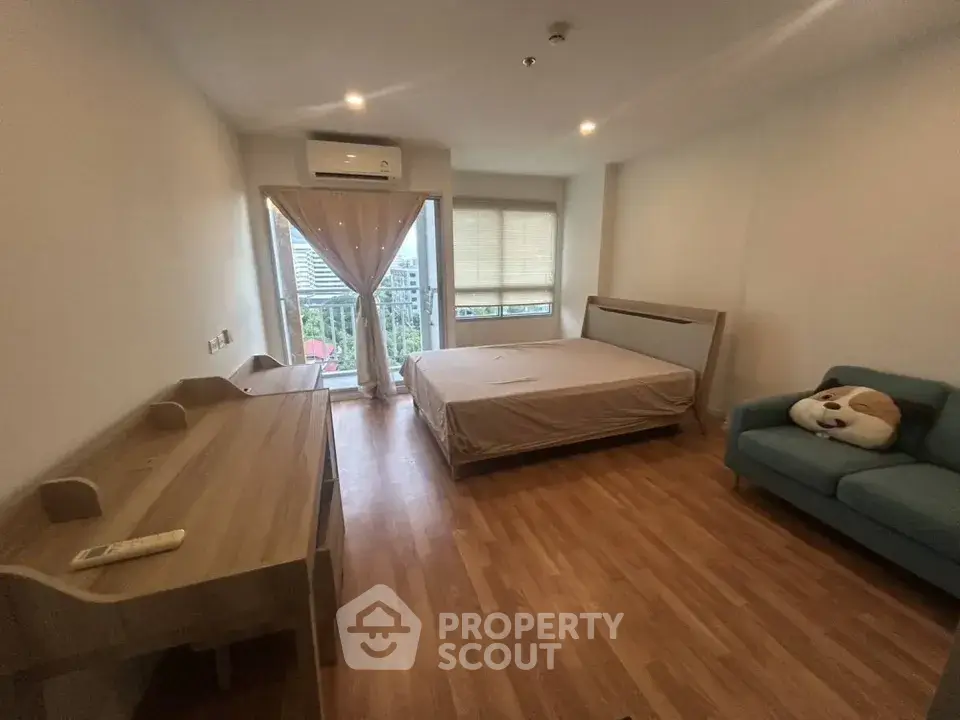 Spacious bedroom with wooden flooring, large window, and cozy seating area.