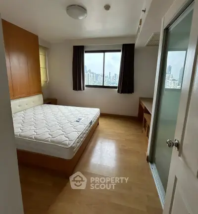Cozy bedroom with city view, wooden flooring, and ample natural light.
