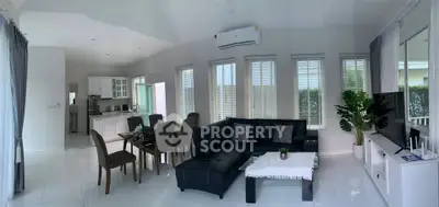 Spacious modern living room with open kitchen, featuring sleek black sofa and large windows for natural light.