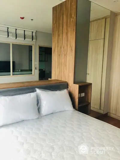 Modern bedroom with stylish wooden accents and cozy white bedding in a contemporary apartment.