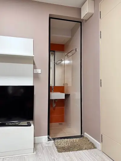 Modern apartment interior with TV and bathroom entrance, showcasing sleek design and functionality.