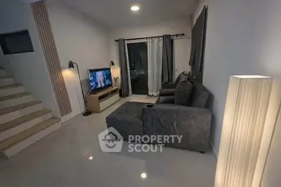 Modern living room with cozy gray sofa and TV, featuring elegant lighting and sleek tiled flooring.