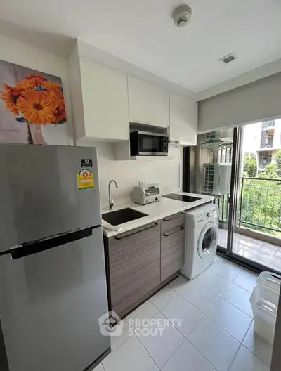 Modern kitchen with balcony view, featuring fridge, washing machine, and sleek cabinetry.