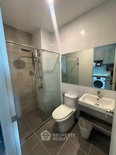 Modern bathroom with glass shower, sleek fixtures, and washing machine view.