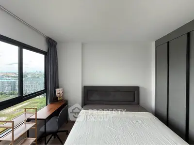 Modern bedroom with large window offering stunning city views, featuring a cozy bed and stylish workspace.