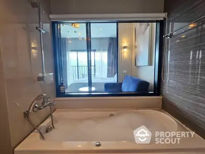 Luxurious bathroom with bathtub and view into modern bedroom with balcony access.