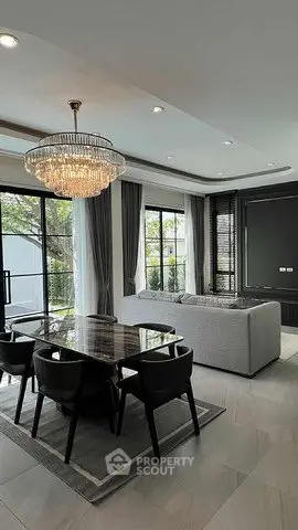 Luxurious living room with elegant chandelier and large windows offering garden views.