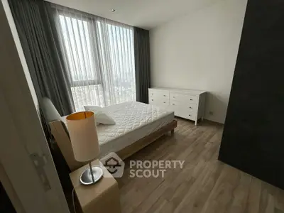 Spacious bedroom with large window and modern furnishings in a high-rise apartment.