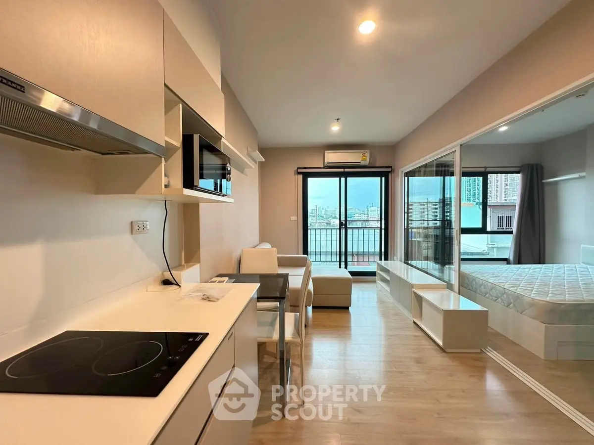 Modern open-plan apartment with kitchen, living area, and bedroom featuring city view balcony.