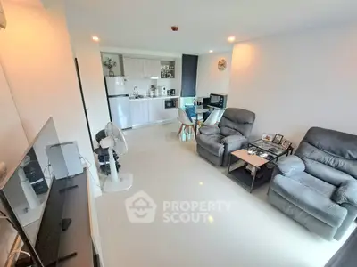 Modern living room with open kitchen, featuring sleek furniture and bright lighting.