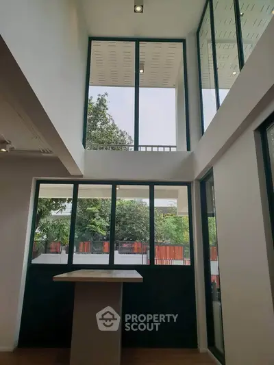 Modern interior with large windows and high ceiling, offering abundant natural light and garden view.