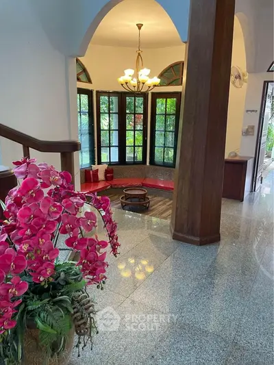 Elegant living room with large windows and floral decor, featuring a cozy seating area and polished flooring.