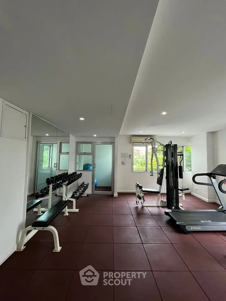 Spacious gym with modern equipment and natural light in a residential building.