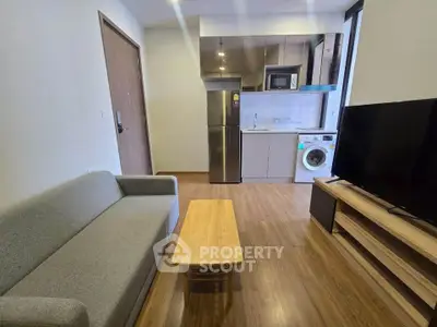 Modern studio apartment with sleek kitchen and cozy living area, featuring a washing machine and stainless steel appliances.