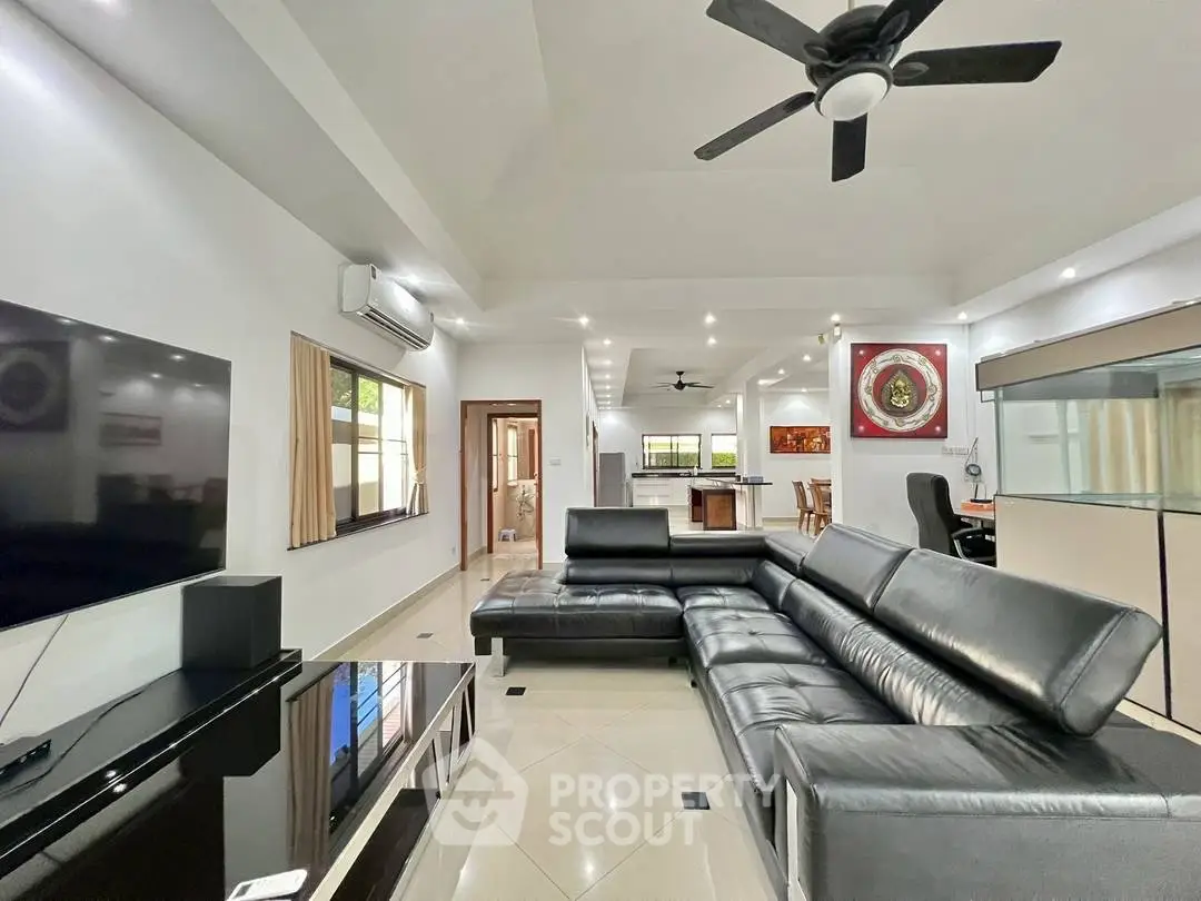 Spacious modern living room with sleek black leather sofa and open kitchen layout.