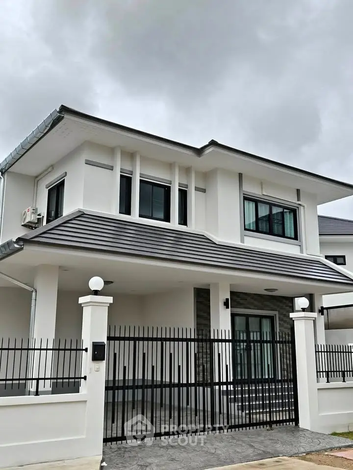 Modern two-story house with sleek design and gated entrance under cloudy sky.