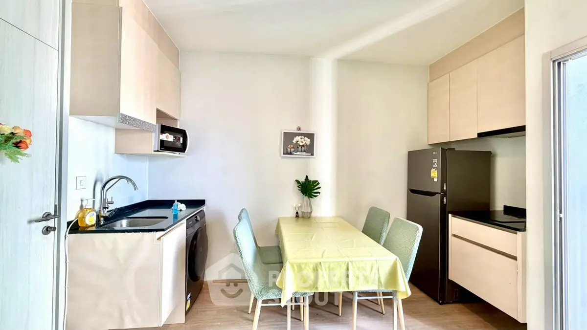 Modern kitchen with dining area, featuring sleek cabinets, a washing machine, and a compact fridge.
