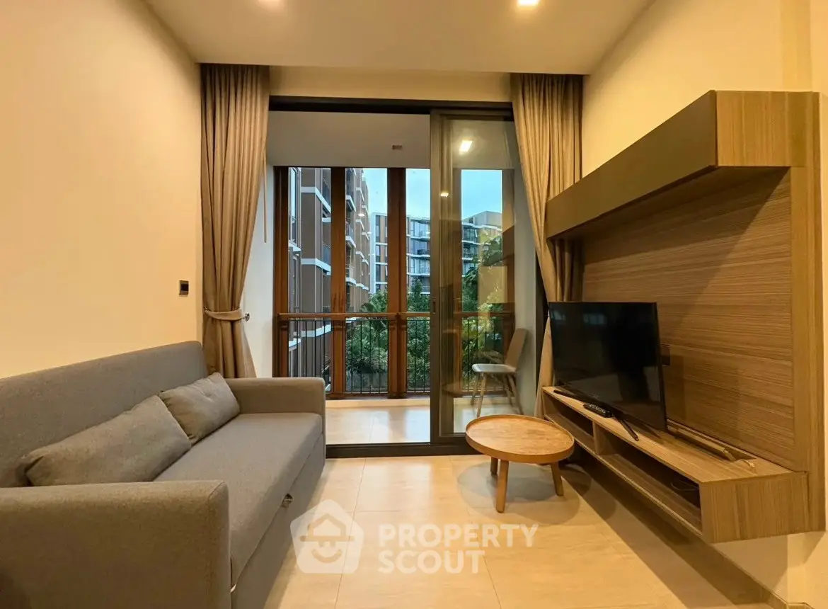 Modern living room with cozy sofa and TV, opening to a balcony with a view of the building exterior.