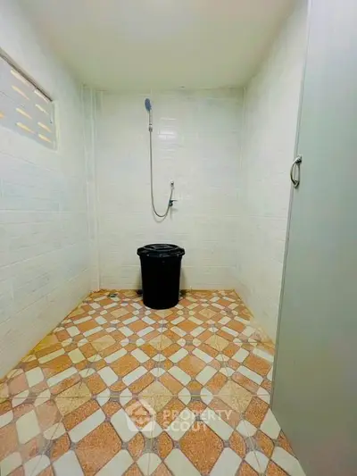 Simple bathroom with tiled floor and shower area, featuring a black bucket for utility use.