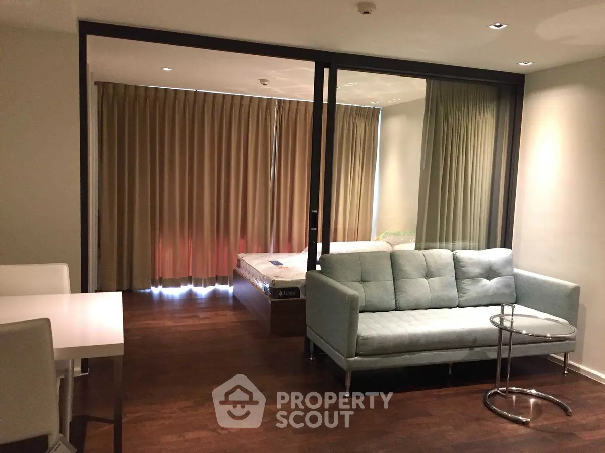 Modern studio apartment with cozy living area and bedroom separated by glass partition.