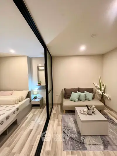 Modern living room with cozy sofa and stylish decor adjacent to a bedroom, featuring elegant flooring and soft lighting.