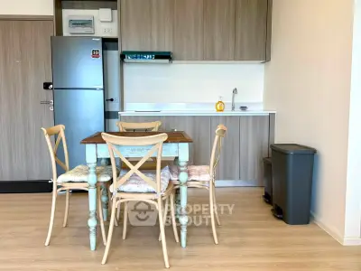 Modern kitchen with wooden dining table and chairs, sleek cabinetry, and stainless steel fridge.