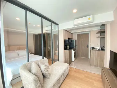 Modern studio apartment with glass partition, cozy living area, and compact kitchen.