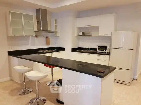 Modern kitchen with sleek black countertops and white cabinetry, featuring a breakfast bar and contemporary stools.
