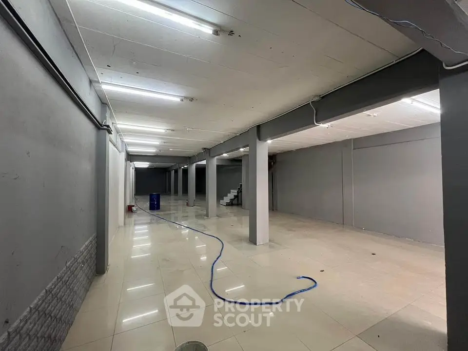 Spacious basement area with tiled flooring and fluorescent lighting, ideal for storage or commercial use.