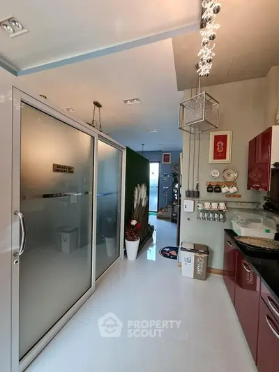 Modern kitchen with sleek red cabinets and frosted glass sliding door, featuring stylish lighting and decor.