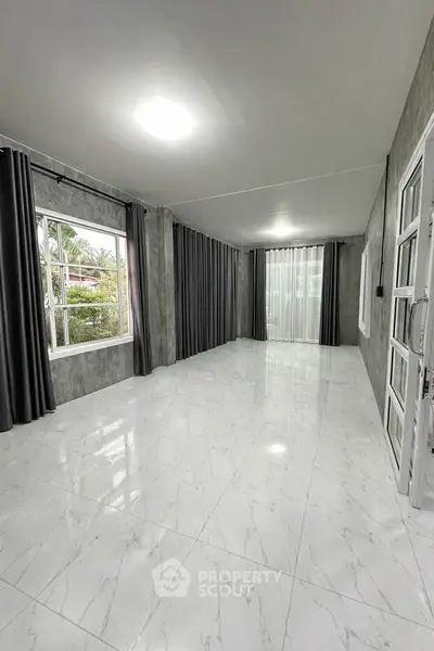 Spacious modern living room with large windows and elegant curtains, featuring sleek marble flooring.